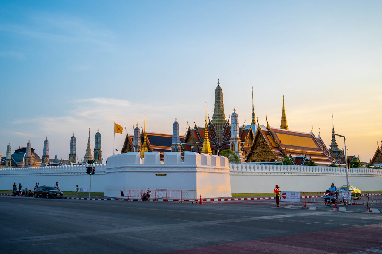 The Grand Palace and Wat Phra Kaew temple spires behind white walls at sunset in Bangkok, Thailand.
